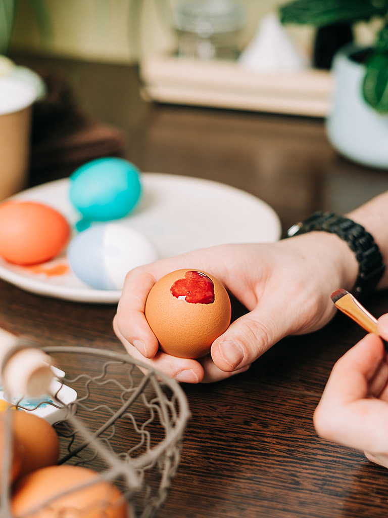 Easter day. Cropped hands of Adult man painting eggs on wooden background. Sitting in a kitchen with crayons. Preparing for Easter, creative homemade decoration